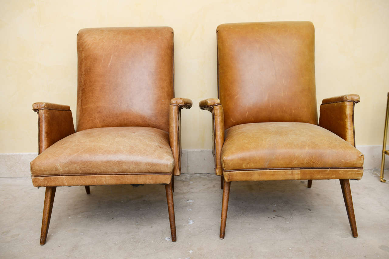 Pair of Mid Century Warmly Worn Leather Chairs;  rectangular back, outset arms with nail head decoration having tapered legs to finish a very sophisticated modern look.