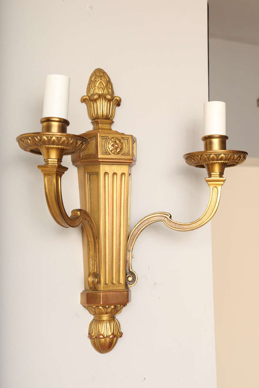 A pair of Louis XVI two-light gilt bronze wall sconces with tapering fluted backs issuing candle arms with leaf tip edge.  Attributed to Edward F. Caldwell & Co, New York 