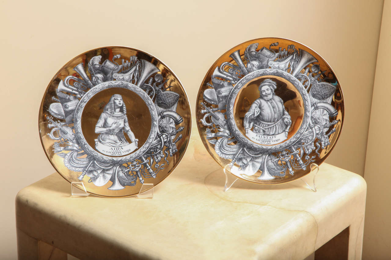 A set of 12 transfer decorated Fornesetti plates from the Melodramma series each in his signature style, the graphic black and white designs depicting characters from 19th century operas, each plate with gold decorated borders having trompe loi