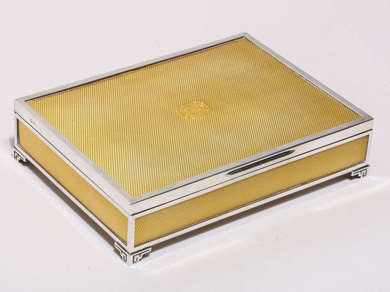 Rectangular box with engine-turned cover and sides under translucent yellow enamel, the cover incorporating a monogram, on bracket feet, gilt interior.
Hallmarks: for 925 silver/ London/ 1929 J.C. (mark of Jacques Cartier)

65.60 ozs. gross.