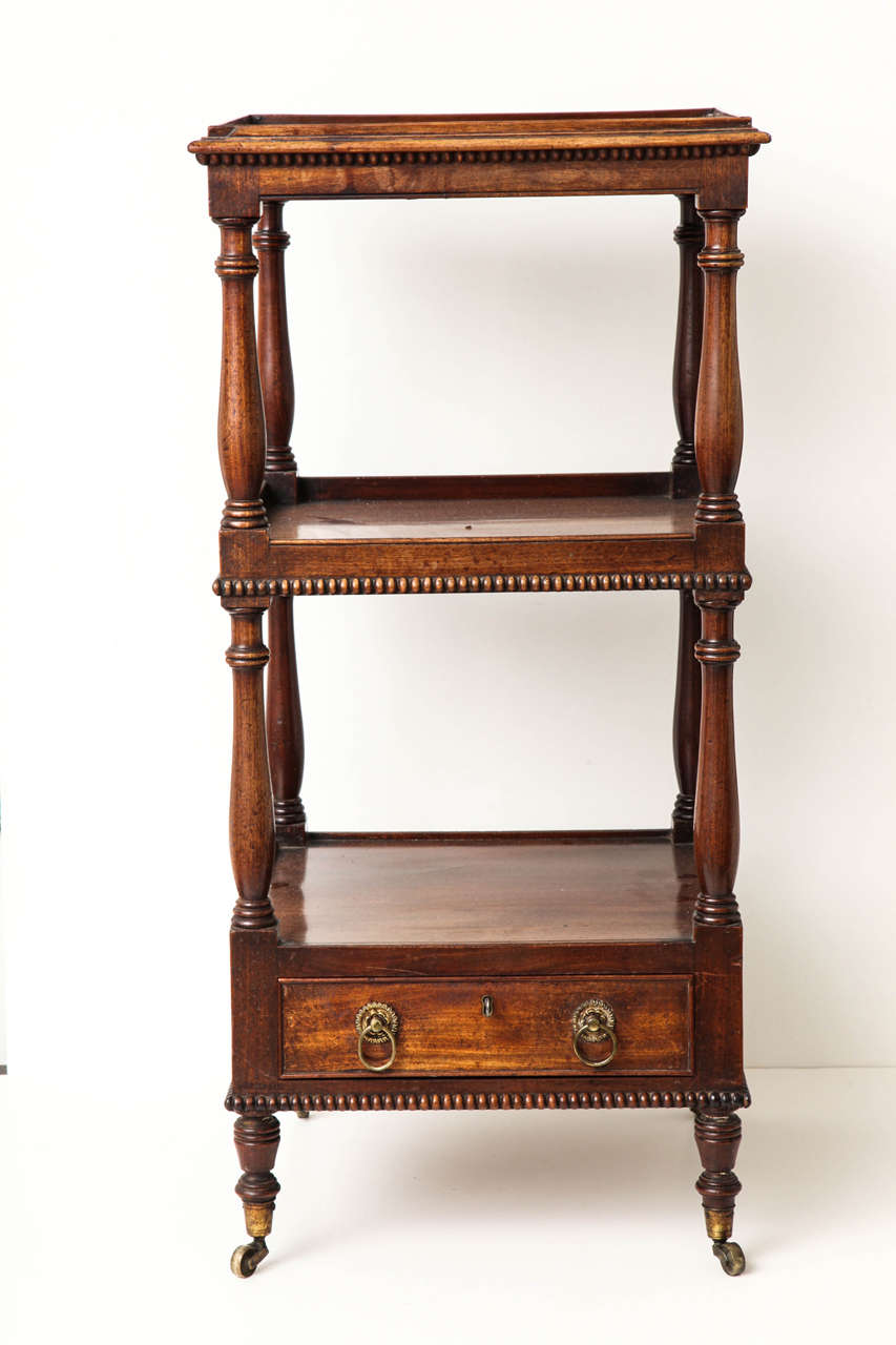 A 19th century English mahogany etagere with two shelves above a lower drawer on turned columns and casters