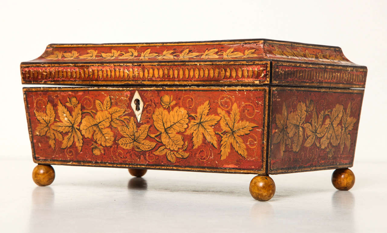 An early 19th century English Regency polychrome red and gilt painted games box with fitted tray interior, the shaped top decorated with trompe l'oeil playing cards, circa 1810