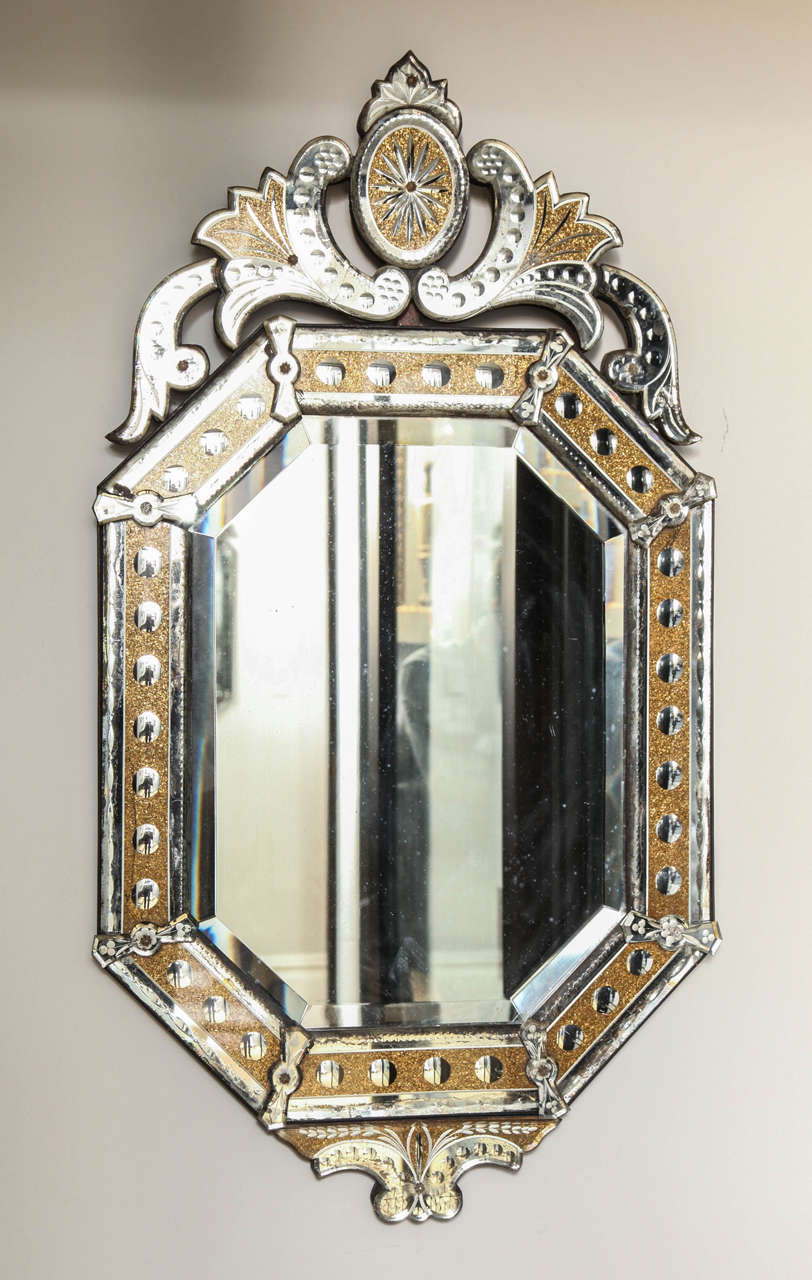 The beveled center glass covered by rectangular sections of mirrored glass frame with oversized bulls eye dots and reverse gilt decoration executed with crushed gold. The upper section surmounted by crest of leaves and scrolls framing an oval