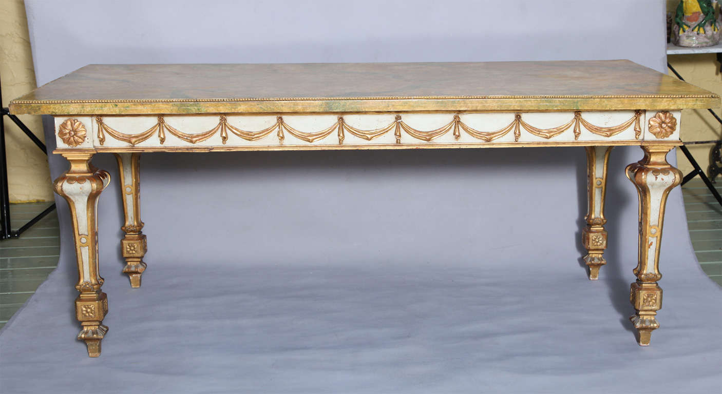 Console table, having a painted and parcel gilt base; its apron decorated by swags, raised on rosette-headed bulbous tapering legs, a later faux-painted top with cock-beaded edge.