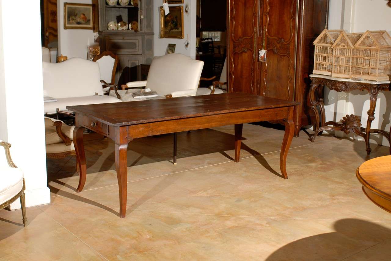A Louis XV style French walnut farm dining room table with single drawer and cabriole legs from the first half of the 19th century. This French farm table features a rectangular planked top, sitting above a simple apron, comprising a single lateral