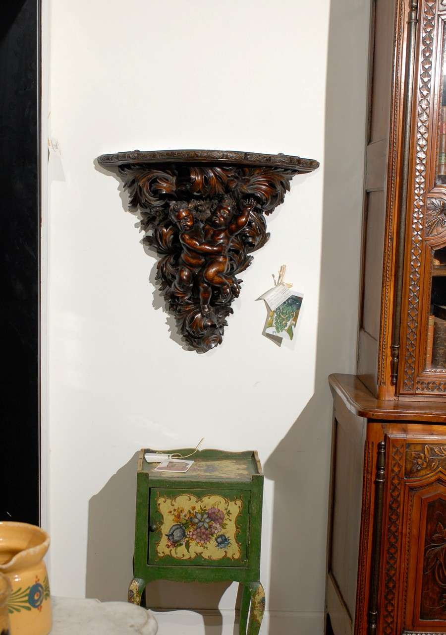 A Baroque style French walnut bracket with hand-carved putti, circa 1800. Born during the tumultuous years of the early 19th century, this French bracket features a semi-circular shaped top, adorned with an ivy carved molding. It it the base,