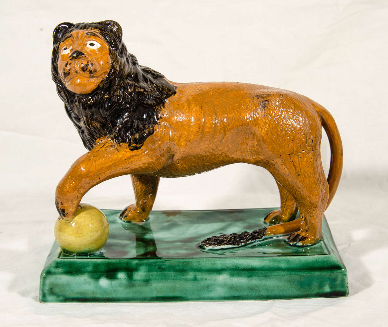 A good antique Staffordshire pottery figure of a standing lion with paw on globe. The modeling of the face is exceptional making this figure very appealing.The figure has a  slightly comical aspect probably not intended at the time of making.