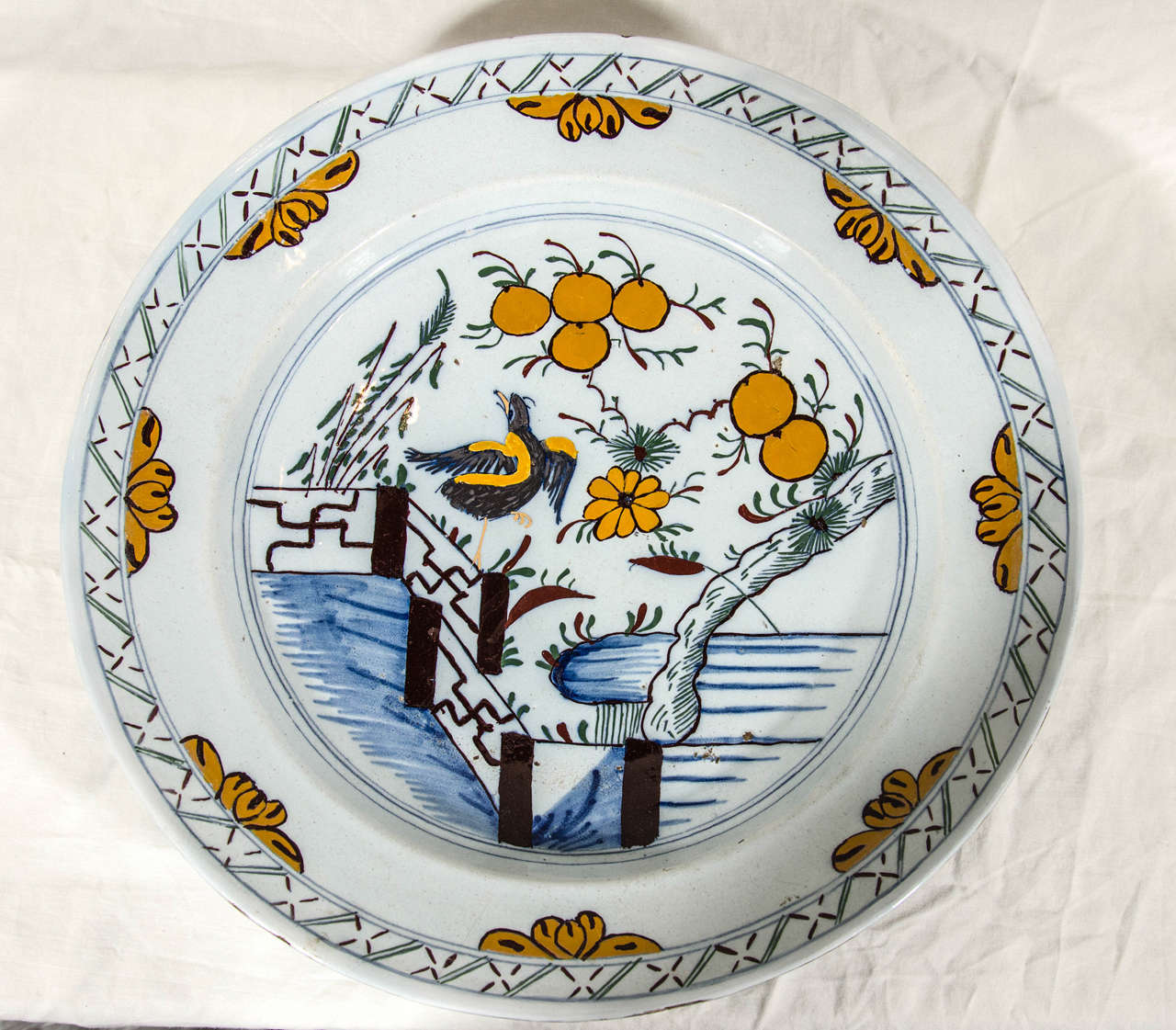 A polychrome Dutch Delft charger with a whimsical scene of a bird dancing under an orange tree. The elements of the design are derived from Chinese porcelain, but the presentation is completely original.