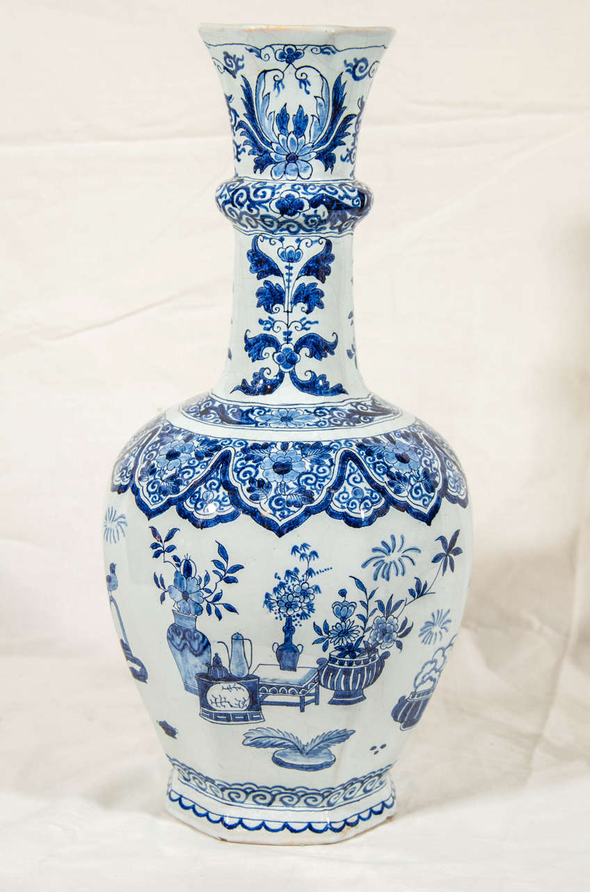 A pair of Dutch Delft Blue and White bottle vases painted in cobalt blue under a light blue glaze. Each vase shows  songbirds, flower filled vases, and other auspicious objects on a garden terrace.
The vases rise from an octagonal base. The base