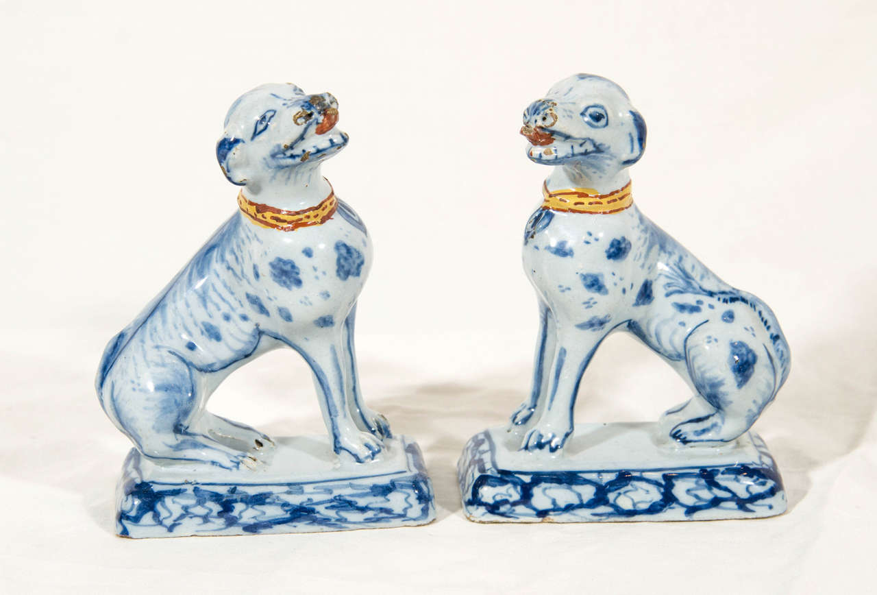 A pair of Blue and White Dutch Delft hounds modeled facing each other and sightly turned to the side. They stand on typically stylized plinths. Each dog has a polychrome red and yellow 