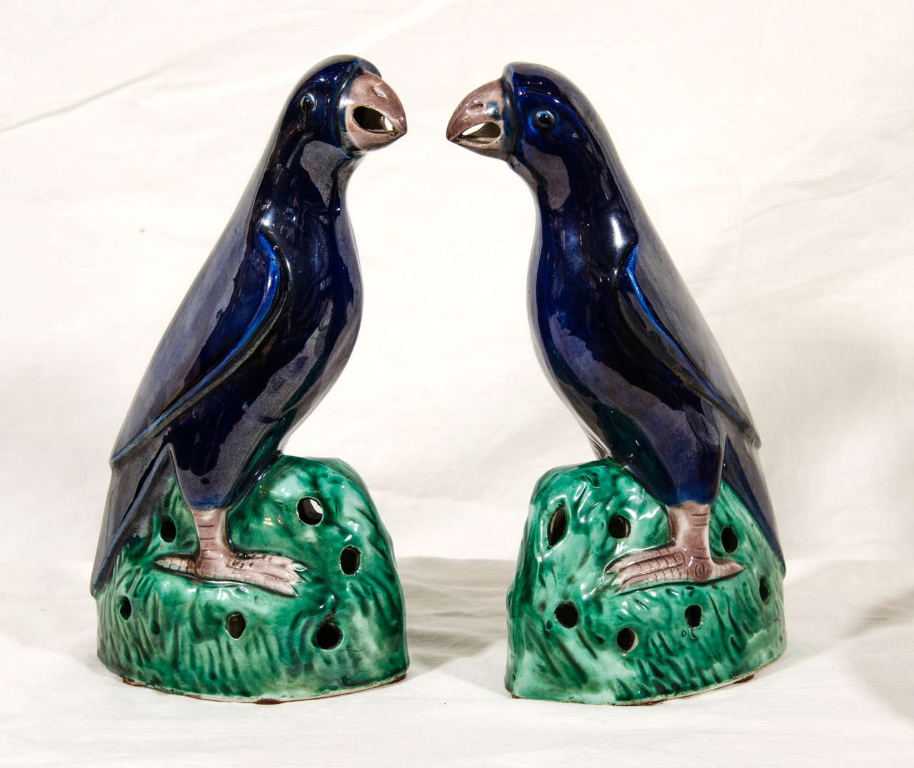 A pair of Famille Verte parrots each modeled in mirror image facing forward with heads slightly cocked. Perched on green pierced rockwork bases, their wings folded, their bodies under a lustrous cobalt glaze.