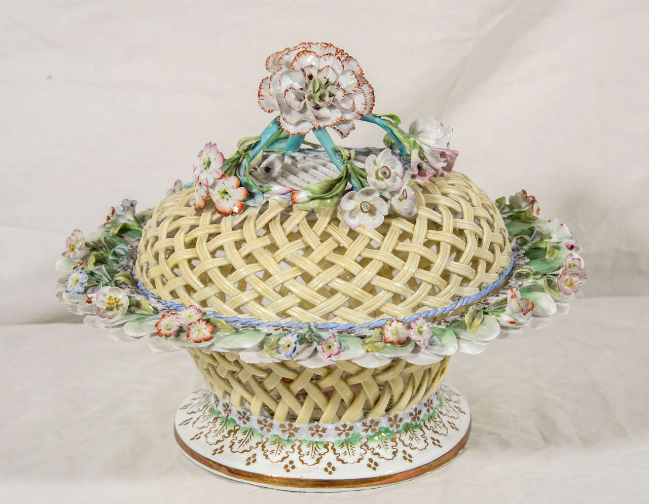 A large porcelain carnation rests on the top of the cover of this Ridgway Porcelain basket. The soft yellow color of the latticework basket is enhanced by the pale pastel colors of the flowers. The interior well is decorated with a bouquet of well