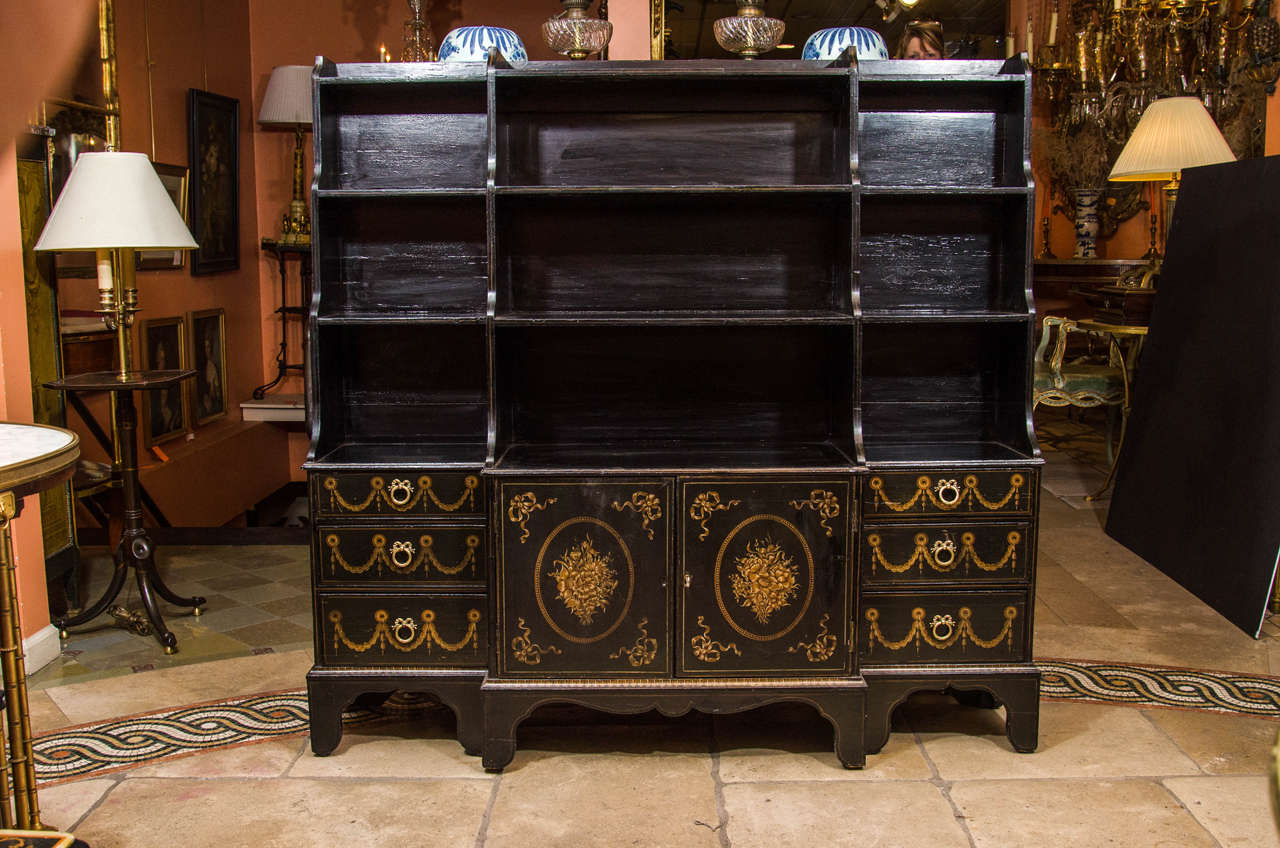 A Regency black painted and swag and bowknot decorated breakfront waterfall bookcase, with graduated shelves over small drawers and central cabinet doors, on shaped bracket feet.