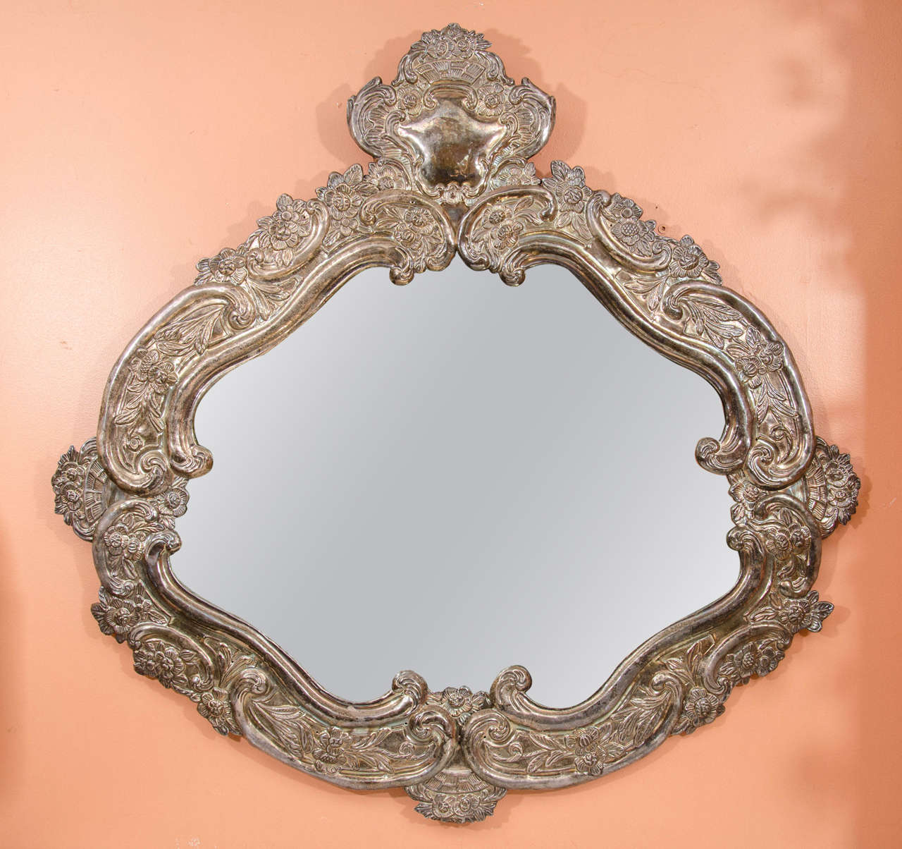 A pair of Portuguese Colonial Baroque silver over brass repousse oval mirrors with C-scroll and floral motifs.