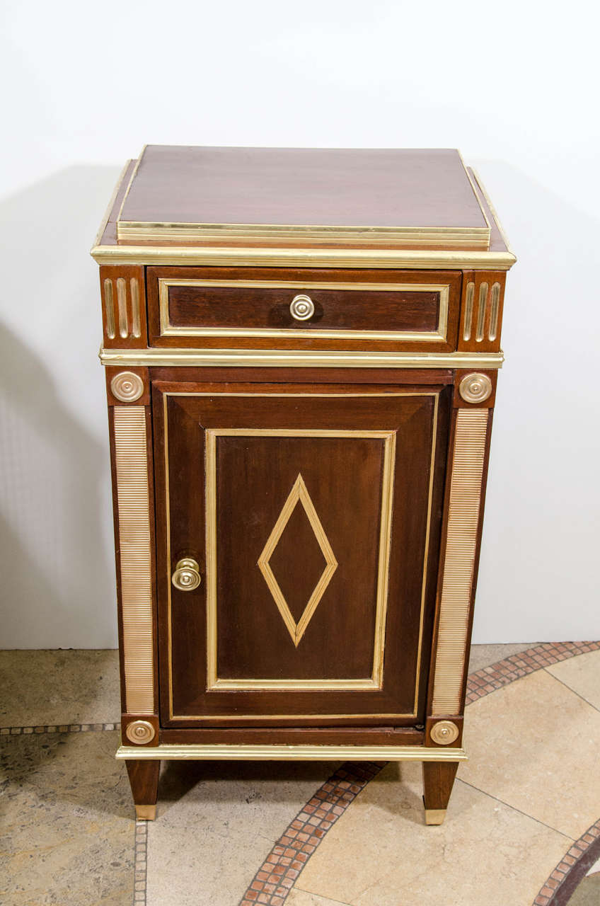 Pair of Russian mahogany and parcel-gilt bedside commodes with brass banded moldings and stepped tops; each fitted with a single drawer over a diamond paneled cabinet door, on tapered square feet.