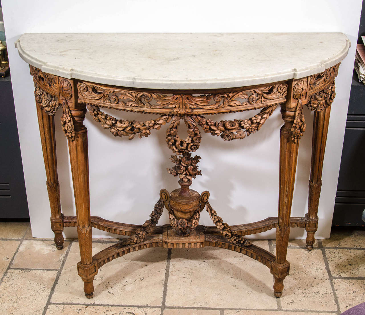 Pair of Louis XVI marble-topped carved beechwood demi-lune console tables, each with pierced foliate scroll aprons and floral garland swags and with floral urn and swags to the stretcher base.