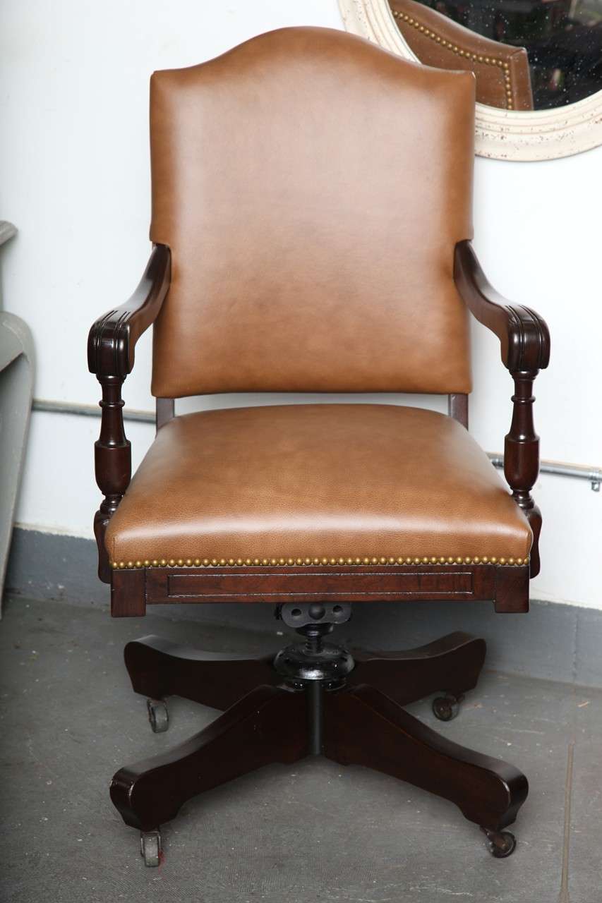 This masculine swivel desk chair with casters has dark cream leather with natural nails and mahogany legs and arms with black coasters. It is the perfect option for an office. 'Mad Men' look. It was recently restored.
