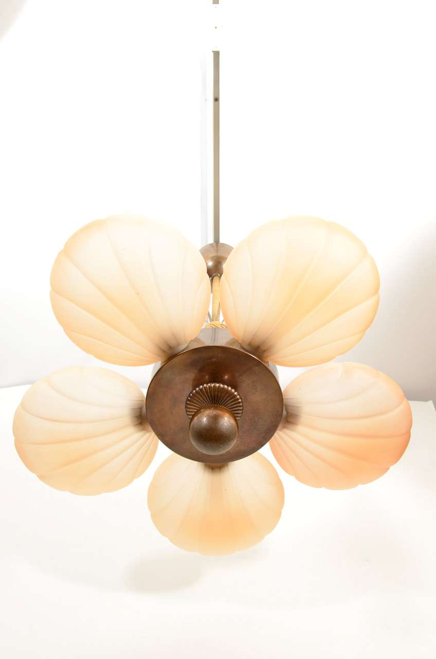 Five peach-toned, frosted and ridged shells attach to the central, bronze disc, with a stylized rosette and circular finial.  Five faceted, peach-toned crystals reflect the light and play along the ceiling. Holds five 40 watt bulbs.