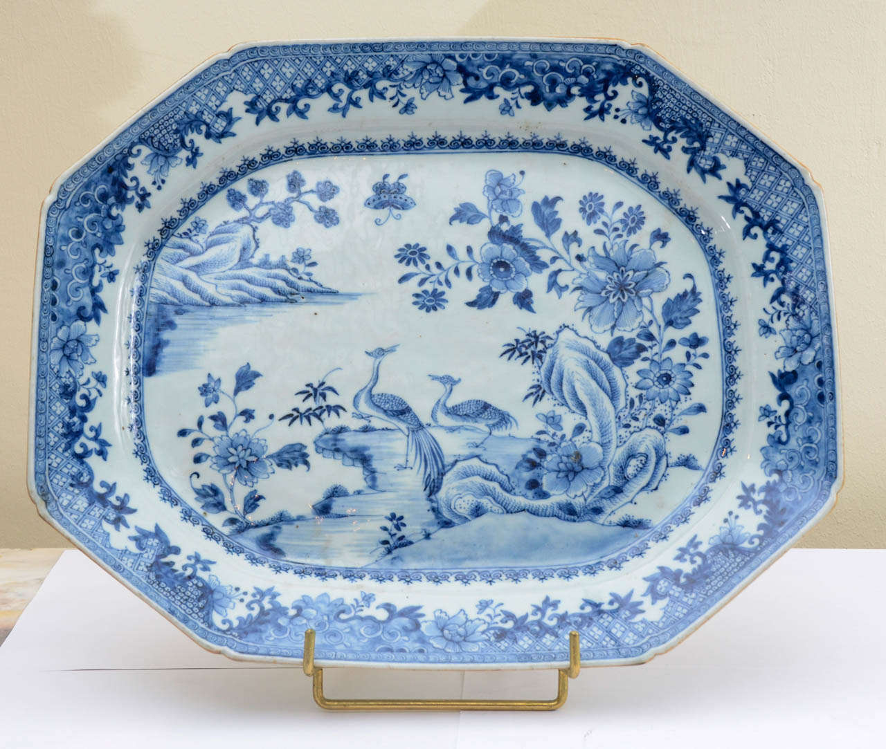 Octogonal porcelain plate, underglazed blue cobalt decor of a peacocks couple on a river bank, and a landscape wooded with blossoming peony trees and longevity pine trees.