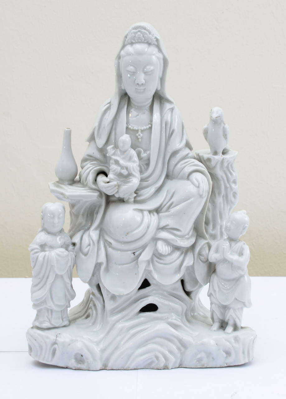 China white DEHUA porcelain representing KUAN YIN godess seated on a rock throne and surrounded by a vase and a phenix with two standing figures at her feet.