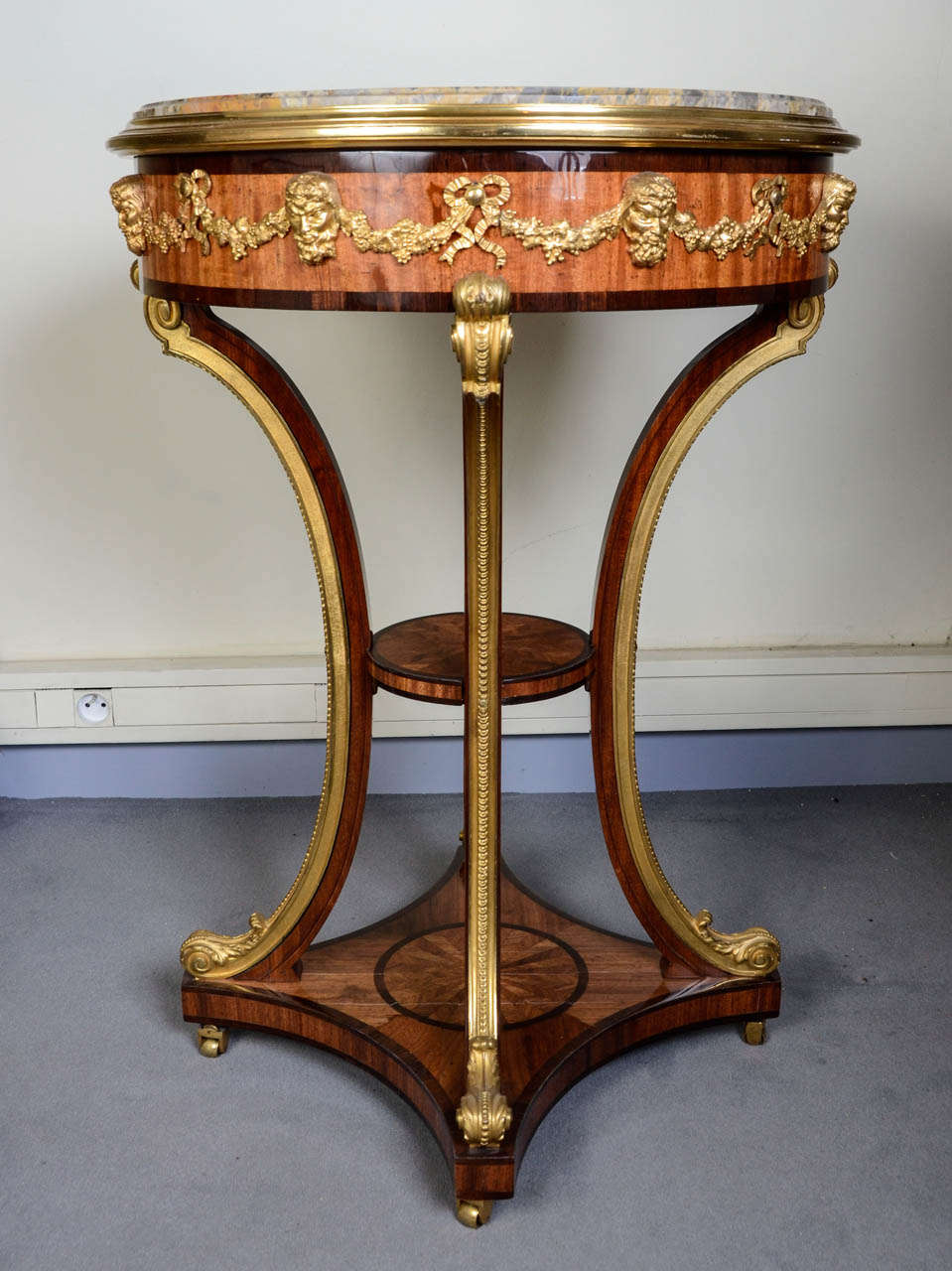 Round gueridon, with a rose beam decor with a rosewood frame and background. Quadripode base in carved and gilded bronze. Two shelves on the legs structure. Breche-like marble. Marble top repaired on the middle.
