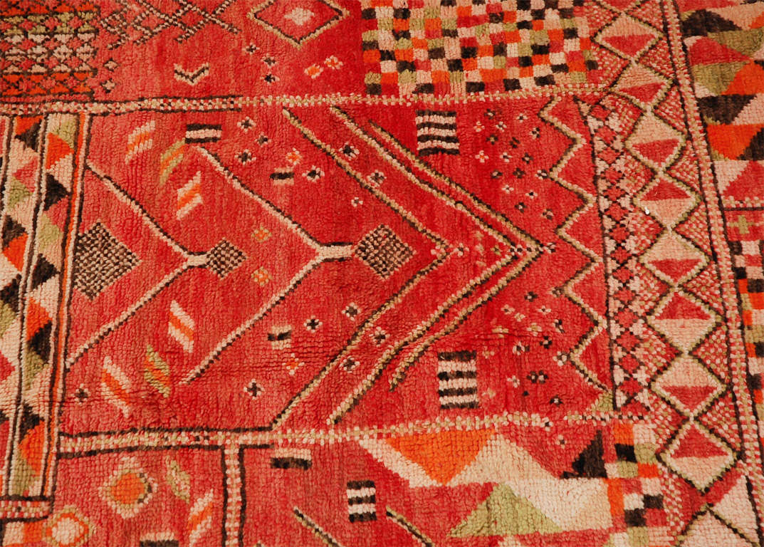 This luscious Moroccan red rug with smatterings of orange, green and black is a room maker. The geometric designs on the rug make it look more contemporary even though it has age.