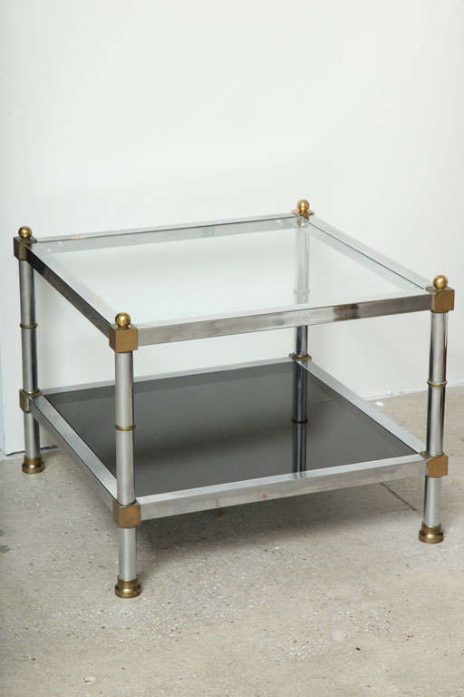 Elegant pair of French Maison Jansen side tables in polished chrome and brass and with original glass tops (Clear glass on top tier with black smoked glass on bottom tier).  Signed Jansen. An elegant and timeless piece to go with any style decor,