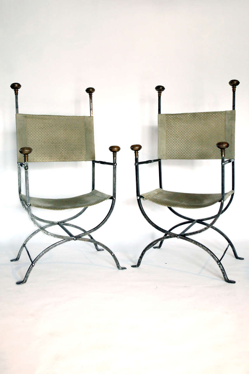 Savonarola style folding chairs with Curule form bases. Backs and seats are gilt embossed taupe suede. Four bronze finials.