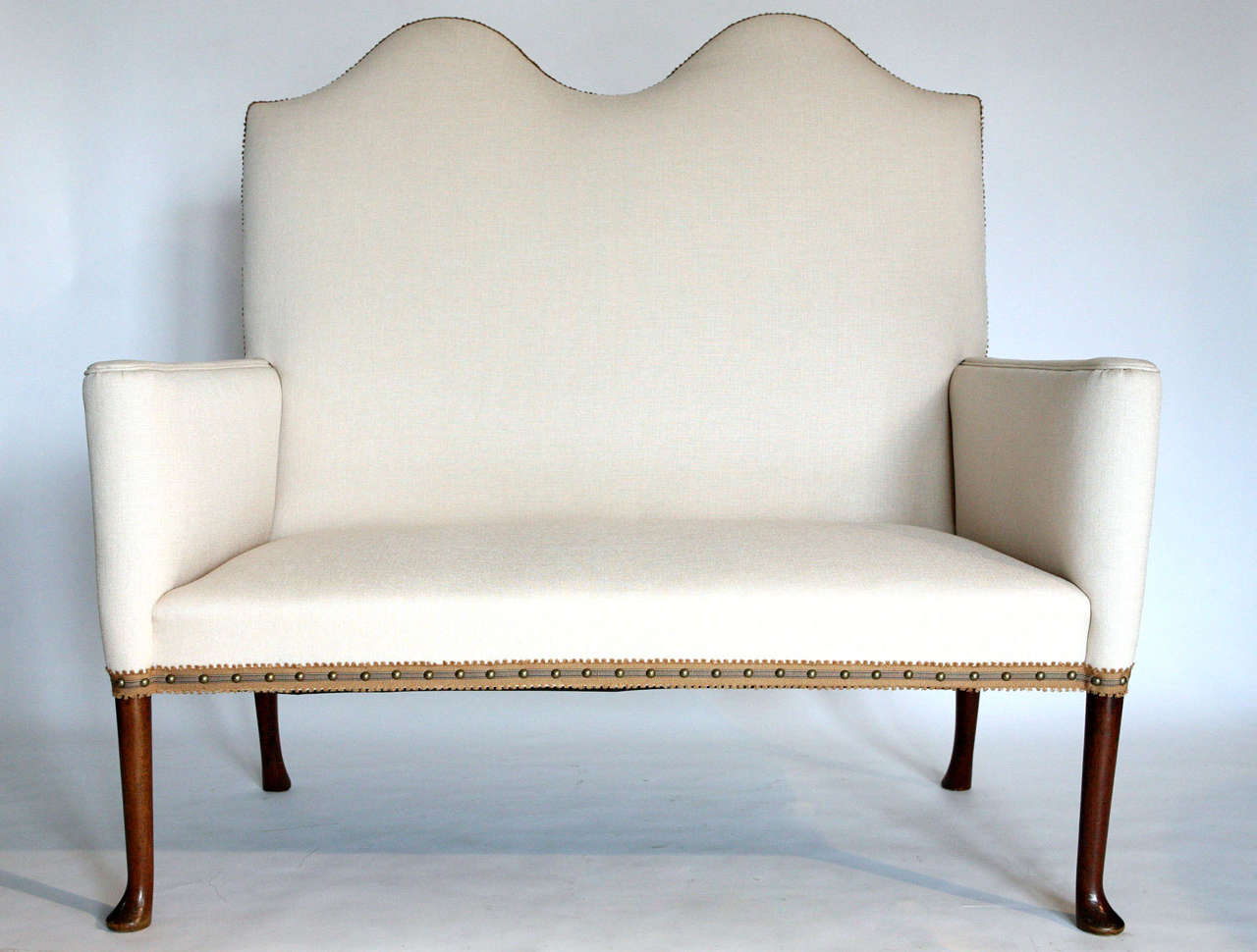 Queen Anne style sofa with pad feet.  Upholstered in cream linen with braid trim and brass studs.