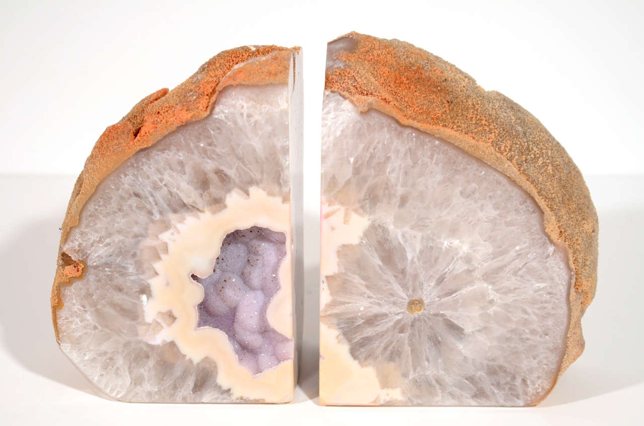 A gorgeous geode with a crystalline center in hues of light violet and  surrounded by creme detailed bands.  The bookends have rough exteriors in natural rustic and sandy hues, and have hand cut and polished centers with crystalized coloration.