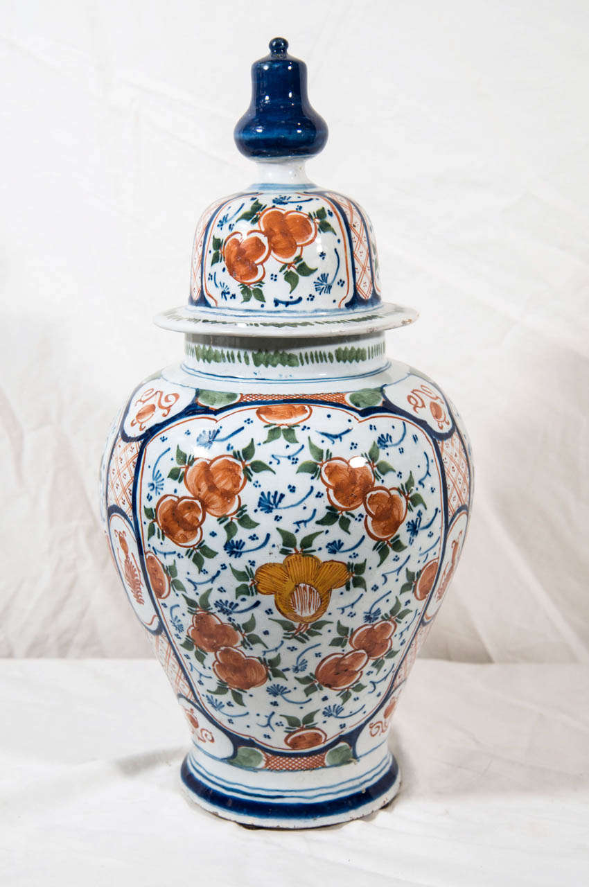 A pair of polychrome Delft ginger jars decorated with an allover foliate design of  green leaves, blue vines, and orange blossoms.