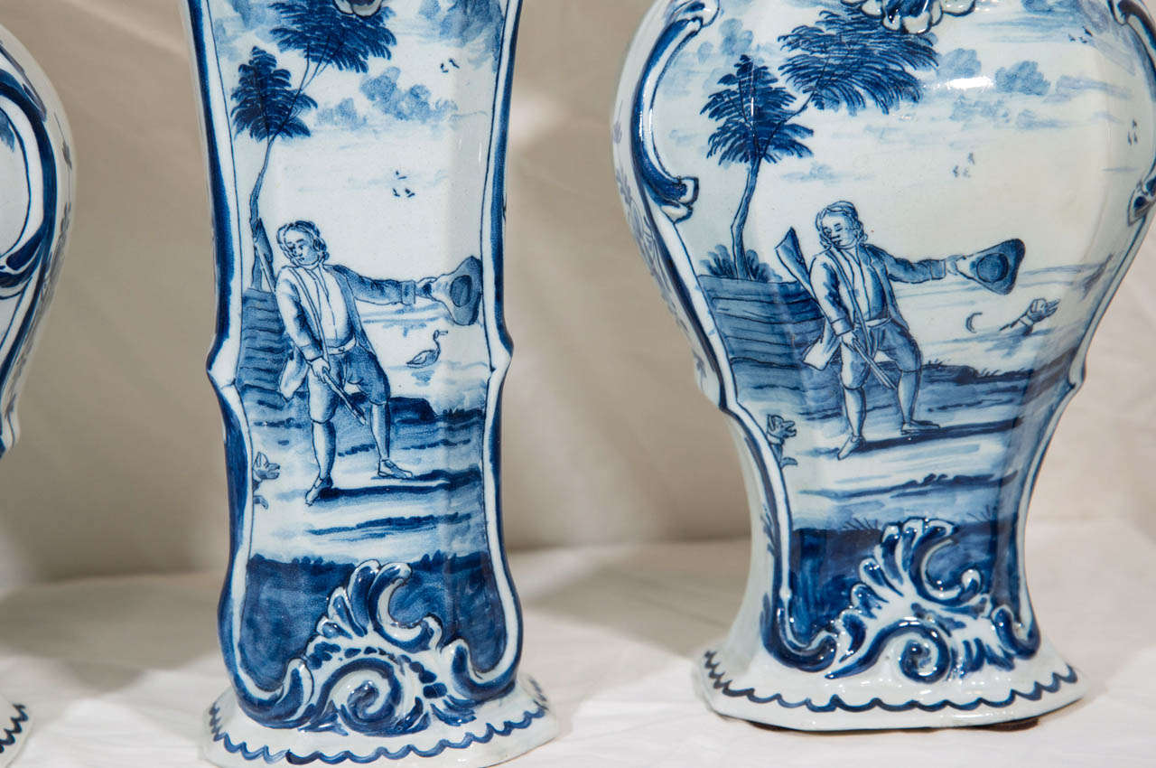 Provenance: The collection of Katherine Mellon.
A fine 18th century five-piece garniture of blue and white Dutch delft vases comprising three baluster vases and two trumpet vases, all with original covers. The decoration shows a European hunt scene