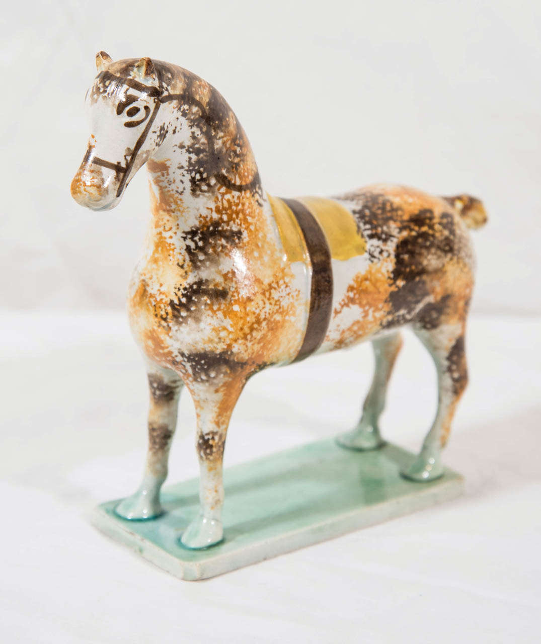 Provenance: With paper label for DM & P Manheim Antiques
An early Staffordshire, Pratt type figure of a horse, sponged and splashed with dappled decoration of manganese and ochre.
He stands on a flat green base with ears pricked and a docked tail.