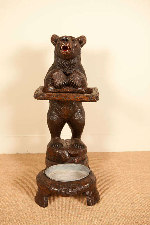 A carved Linden Wood umbrella/cane stand, modeled as a bear cub supporting a retangular branch form with a tin drip pan