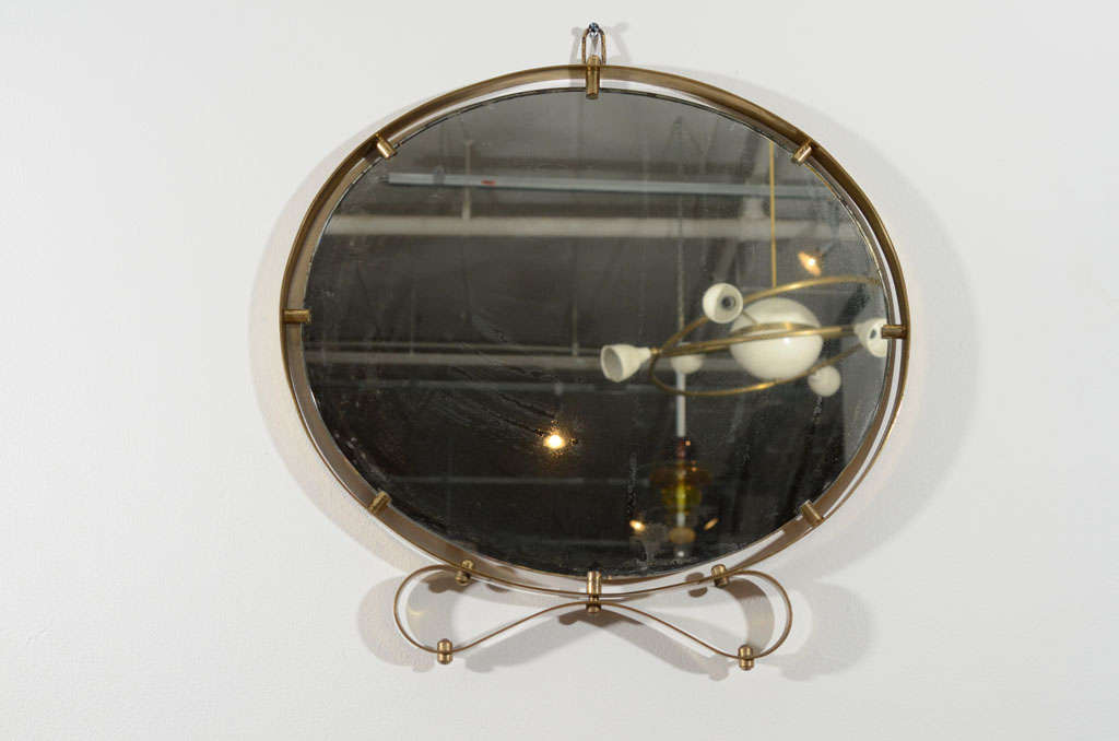 Oval mirror with brass ribbon frame and decorative pegs.