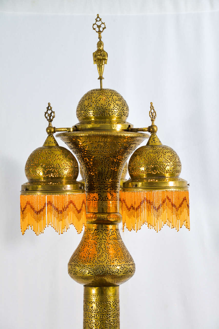 Moroccan pierced brass floor lamp featuring three lamps at the top and wired with lights in the bottom. Beaded fringe has been added in recent years.