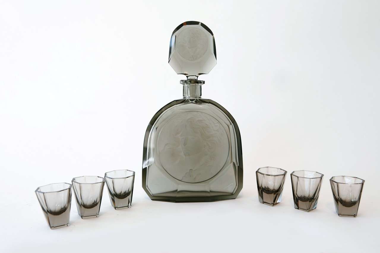 A striking Czech cut glass decanter with six Schnapps glasses of smoked glass. The decanter is decorated with a cameo of a woman in frosted glass on the front of the bottle as well as the stopper. Dimensions below are for the decanter. The Schnapps
