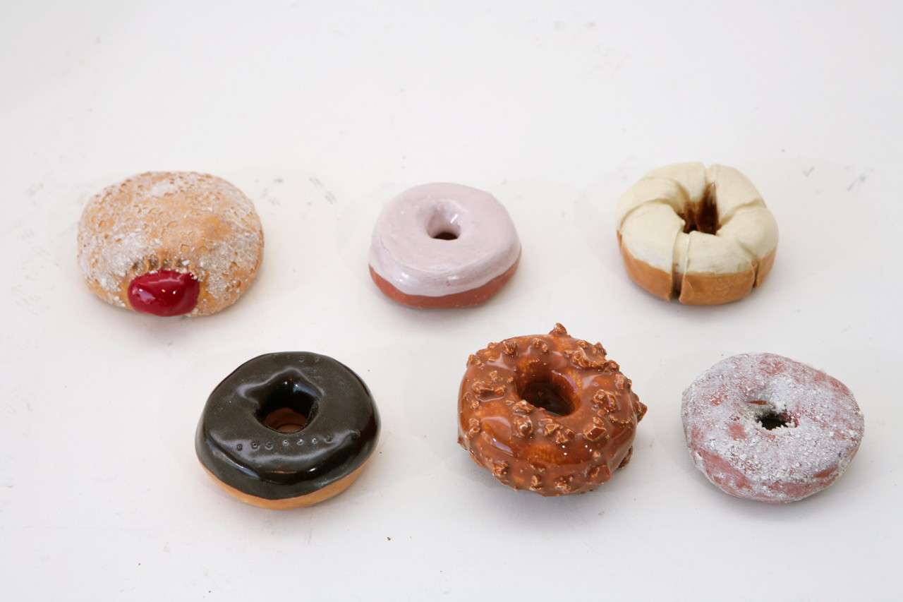 A charming pop art box of a half dozen doughnuts rendered in hand glazed pottery. The doughnuts (chocolate & strawberry glazed, vanilla glazed cruller, powdered, jelly and crumb), which measure approximately 3