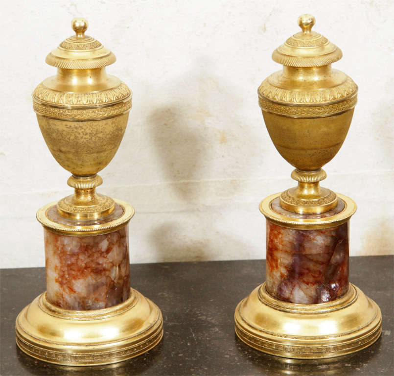 This fine pair of English George III period gilded bronze lidded urns with finely chased neoclassical decoration are raised on plinths composed of specimen Blue John (Derbyshire fluor spar) with gilded bronze mounts.