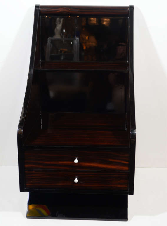 Art Deco end table with sleigh design in the manner of Ruhlmann. It is bookmatched Macassar wood with black lacquer accents that sit atop a black lacquer plinth base with white enamel pulls. It has two drawers and a shelf for displaying books, etc.