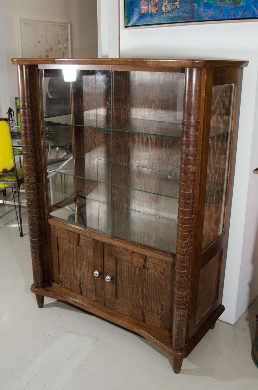 Cerused or limed wood is always in style. This lightly cerused deco cabinet has glass sliding doors and two glass shelves. The bottom has two doors with silver knobs that provide hidden storage. Can be used as a display case for retail or at home to