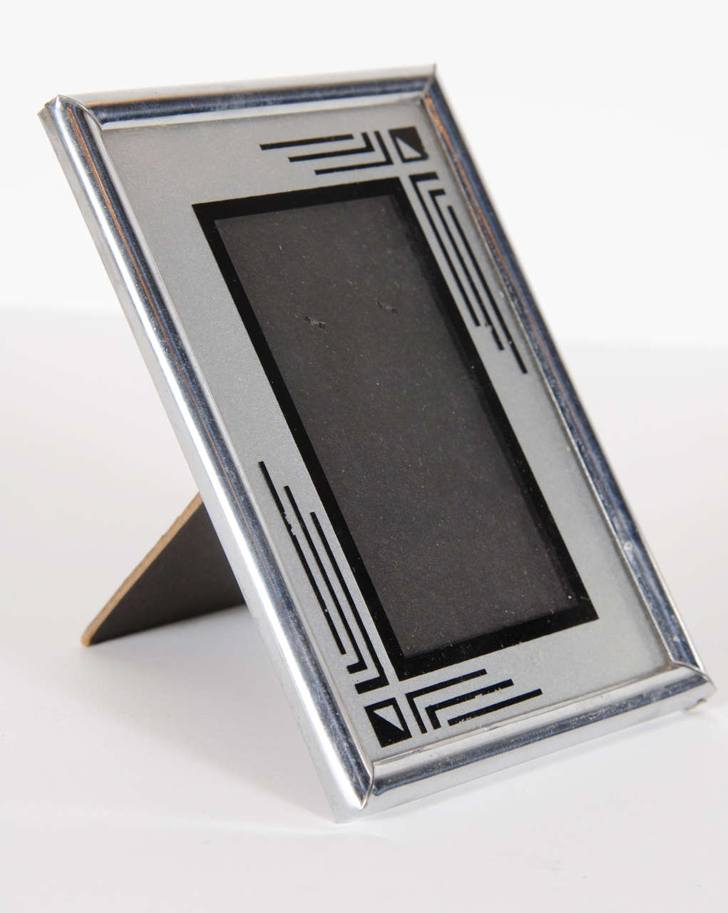 This chrome frame features a highly styled and bold geometric Art Deco design in reverse painted. It is designed for a photograph in size 3 by 5 to be used vertically.
