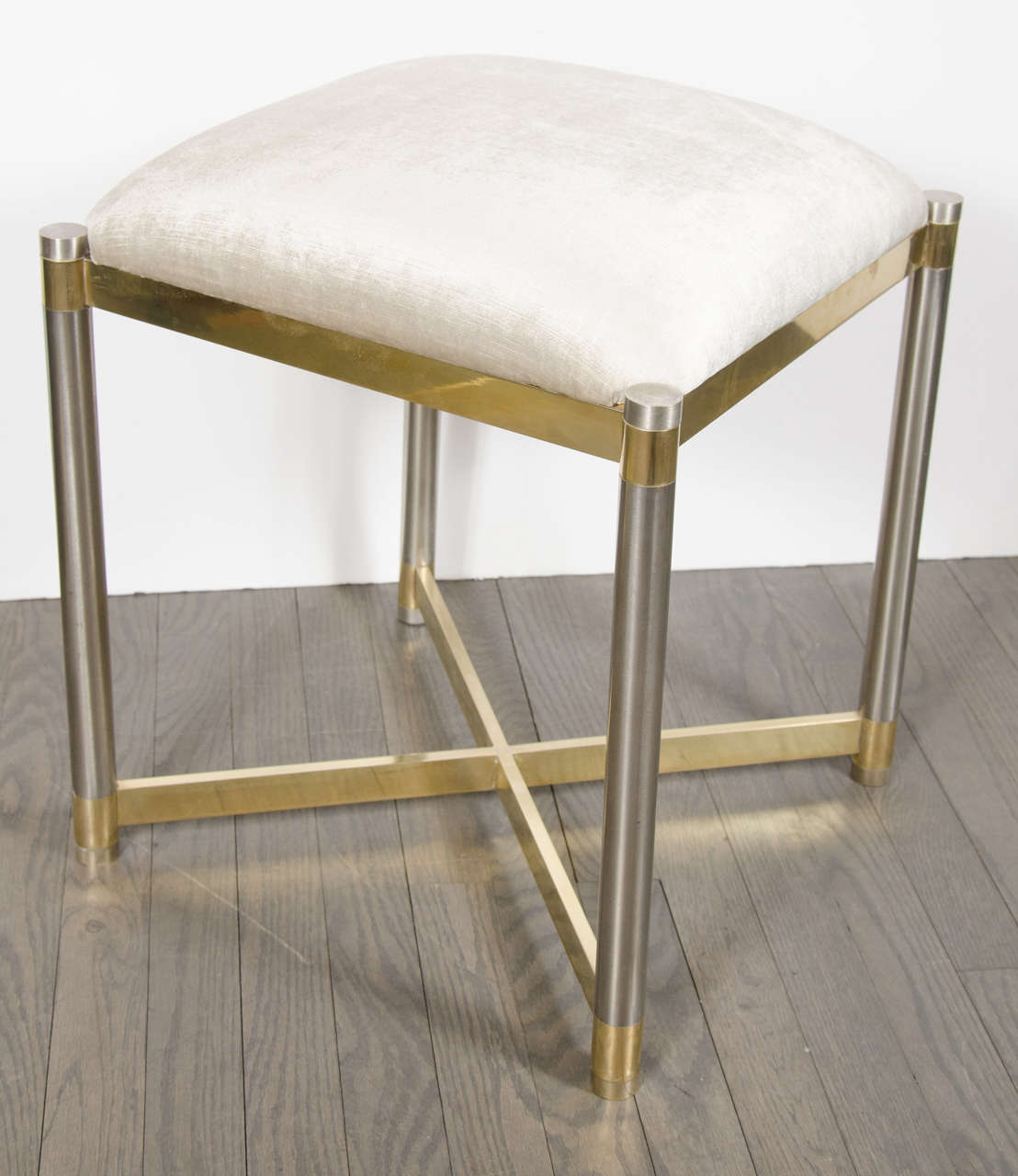 This sophisticated Mid-Century Modernist X-form stool in the manner of Karl Springer was realized in the United States, circa 1970. It features brushed cylindrical chrome legs banded in brass with a brass X-form support at its base and a rectangular