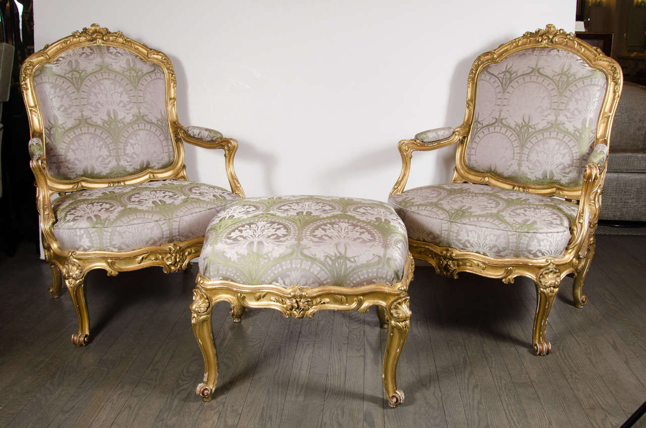 An elegant pair of French bergeres chairs with a matched ottoman in gilded wood and satin upholstery: These chairs are traditionally designed to be very comfortable, the seat frame being over-upholstered, while the rest of the beautifully carved and