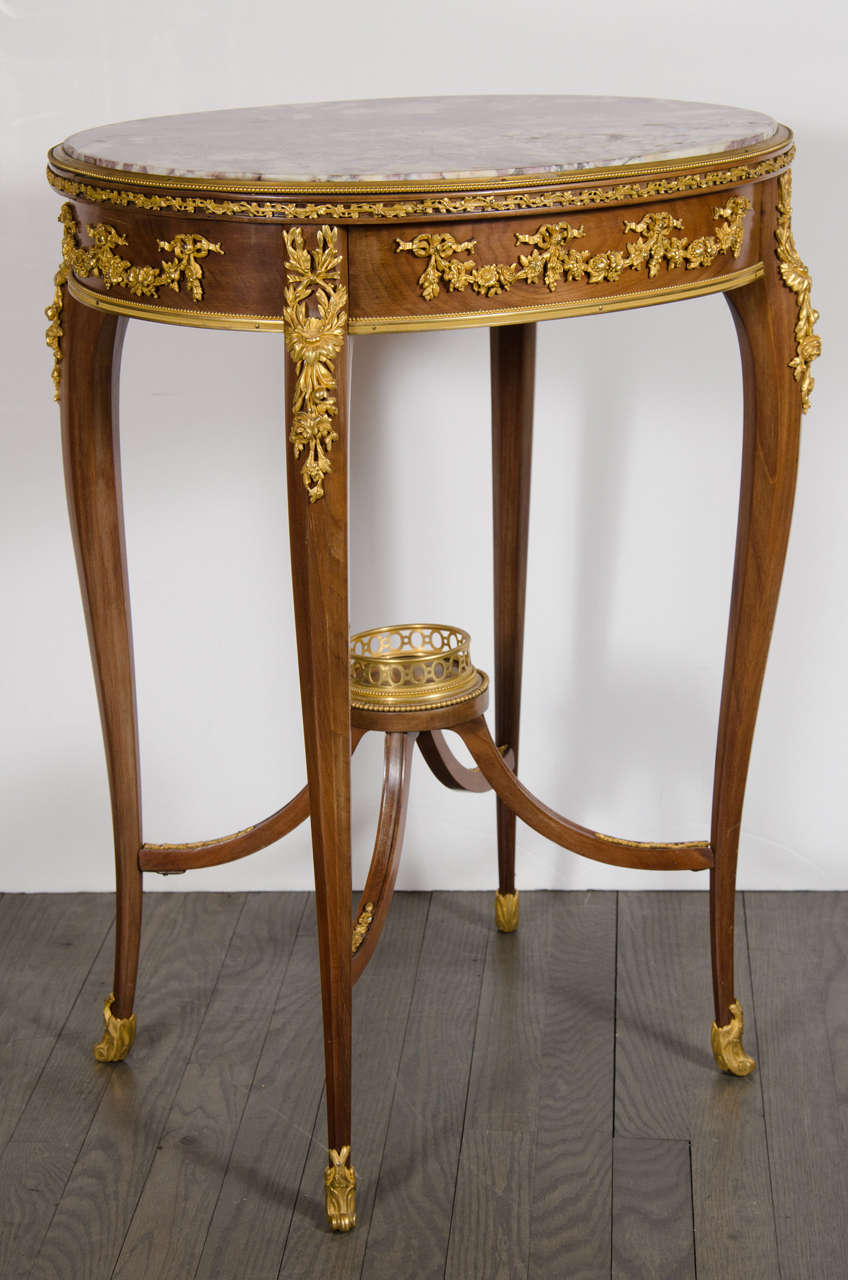 This very elegant table features exquisite bronze ormolu detailing in stylized wreaths, garlands and bows throughout. It also has an exotic marble top with gorgeous coloring and veining. It is made of fine rosewood and also features an exotic wood