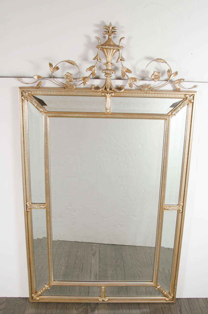 1940s Hollywood Regency pediment mirror in hand-gilded moon-glow finish. This elegant pediment mirror features a top crown consisting of a stylized foliage design that drapes off of its fleur-de-lys style centerpiece. The center mirror panel has a