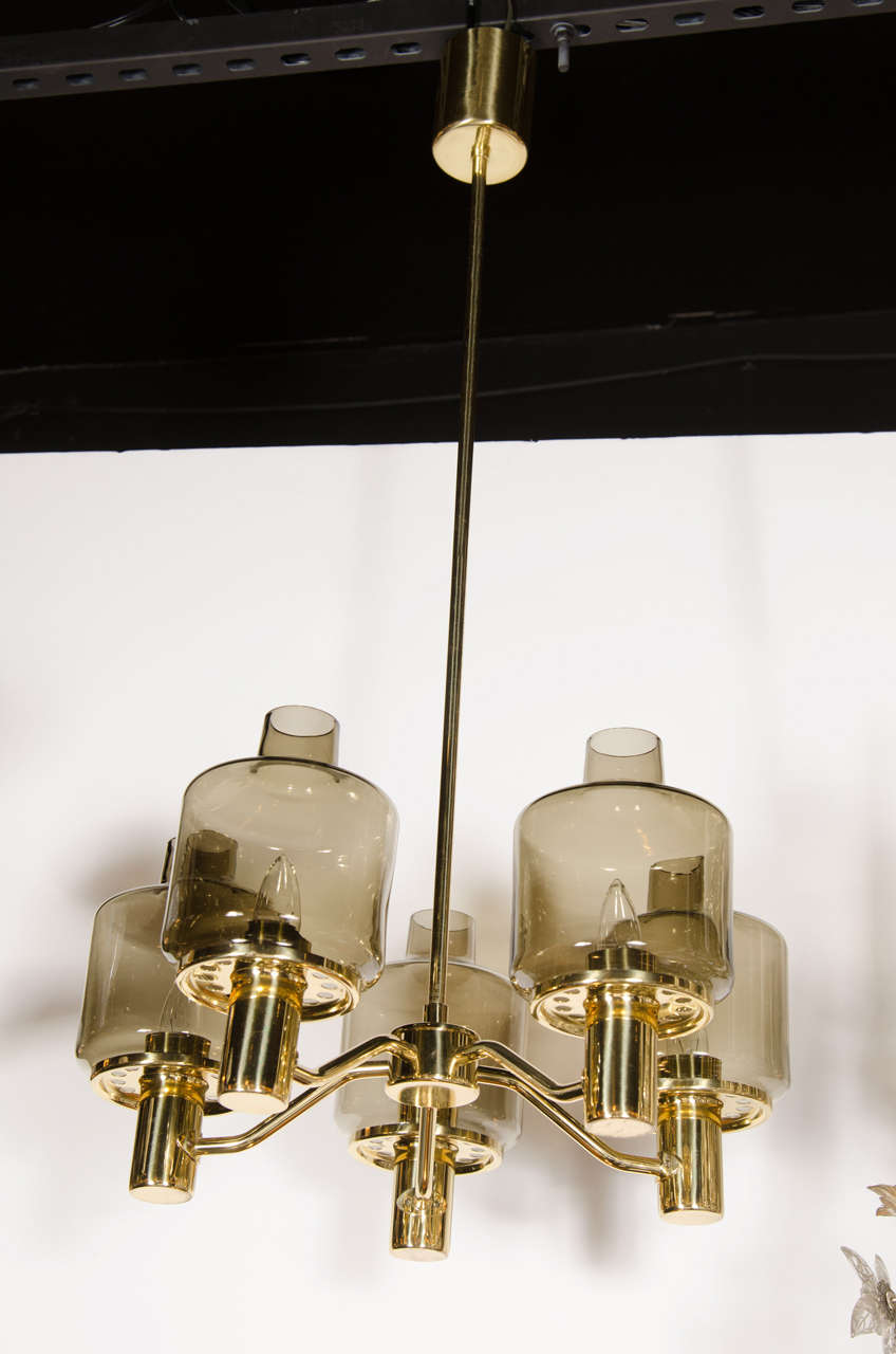 This sophisticated Mid-Century Modern chandelier was realized in Sweden by the celebrated designer of the period- Hans-Agne Jakobsson, circa 1960. It features five lantern style shades in smoked glass with drum form bodies from which a smaller open