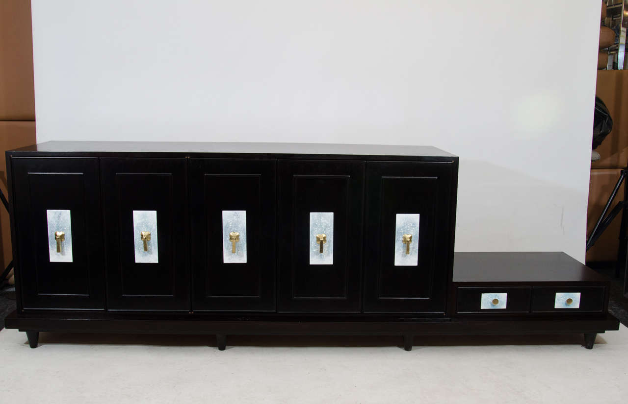 Elegant credenza with an attached low table by Renzo Rutili. The credenza is in an ebonized finish with beautiful enameled escutcheons accented with brass door pulls. The credenza has one cabinet fitted with drawers. Please contact for location. 