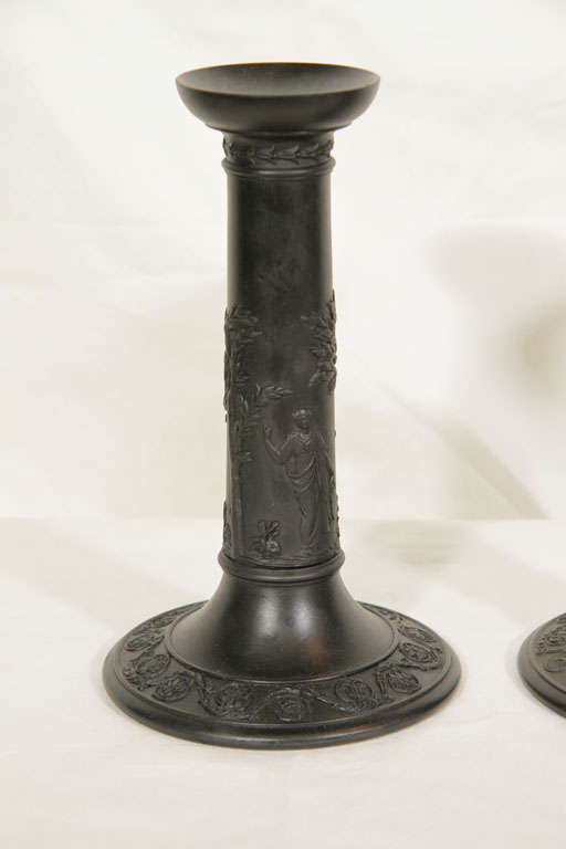 Two pairs of Wedgwood Black Basalt candlesticks cylindrical in form they have classical figures and  borders of scrolling vines.<br />
 Black Basalt was created by Josiah Wedgwood in the 18th century. Wedgwood transformed Egyptian Black, a