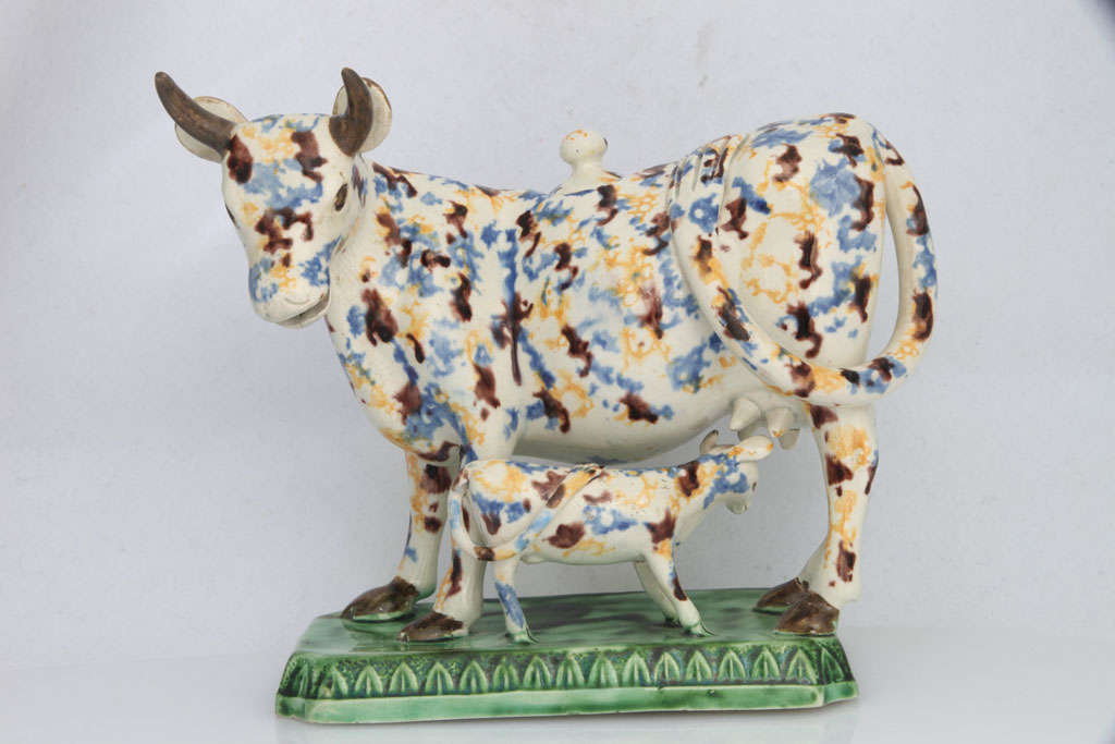 A rare English creamware cow creamer with calf, decorated in underglaze colors on a raised base